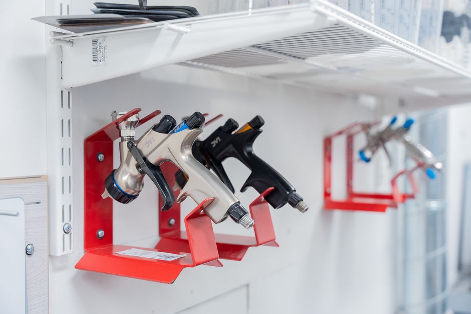 Three spray guns neatly organized on red wall mounts in a well-lit workshop setting.